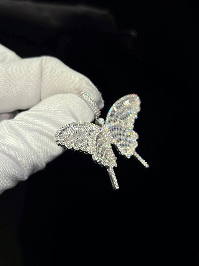 May include: A silver butterfly pendant with sparkling, clear gemstones. The pendant features intricate detailing on the wings and body, with a small loop for a chain. The butterfly design is a popular jewelry motif.
