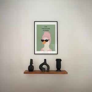 Puede incluir: Una impresi&oacute;n art&iacute;stica enmarcada con un ganso con gafas de sol y una toalla rosa, con el texto "I lied. I won't be ready in 5 minutes." Debajo, una estanter&iacute;a de madera exhibe tres jarrones de cer&aacute;mica negros.