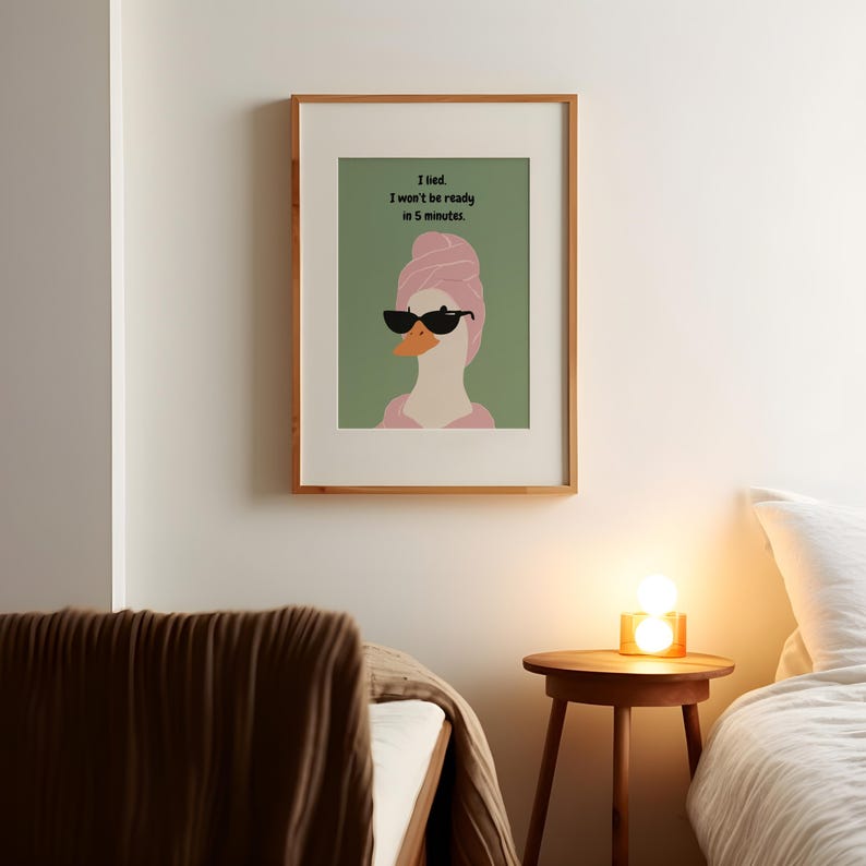 Puede incluir: Impresi&oacute;n art&iacute;stica enmarcada que presenta un ganso de dibujos animados con gafas de sol y una toalla rosa en la cabeza. La impresi&oacute;n tiene el texto "I lied. I won't be ready in 5 minutes." La obra de arte se exhibe en un dormitorio.
