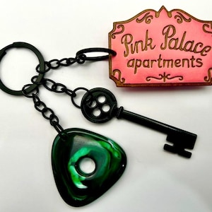 Coraline inspired pink palace keychain with black button skeleton key and green seeing stone image 1