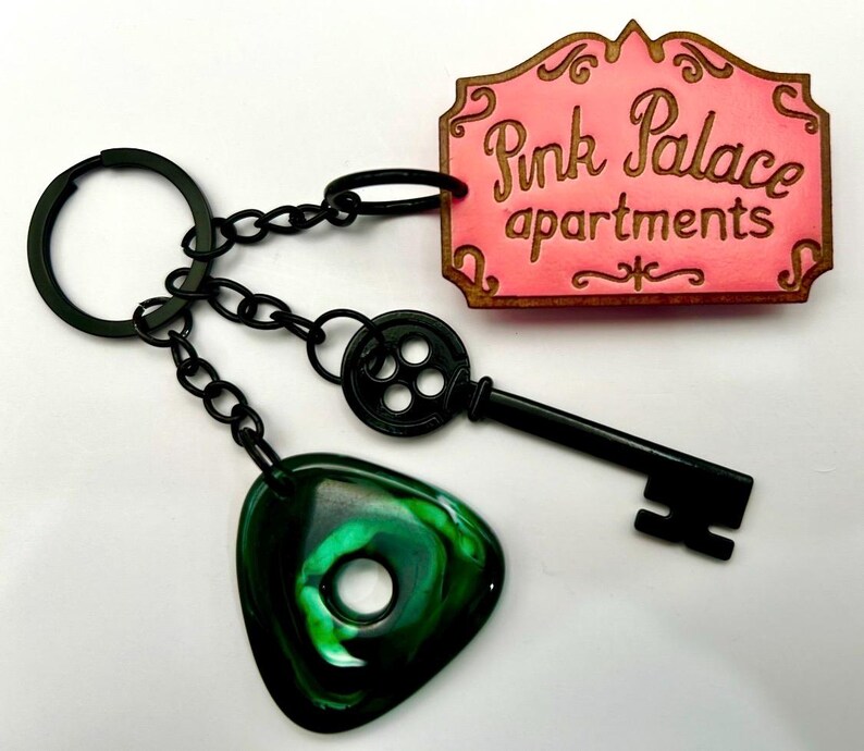 Coraline inspired pink palace keychain with black button skeleton key and green seeing stone image 1