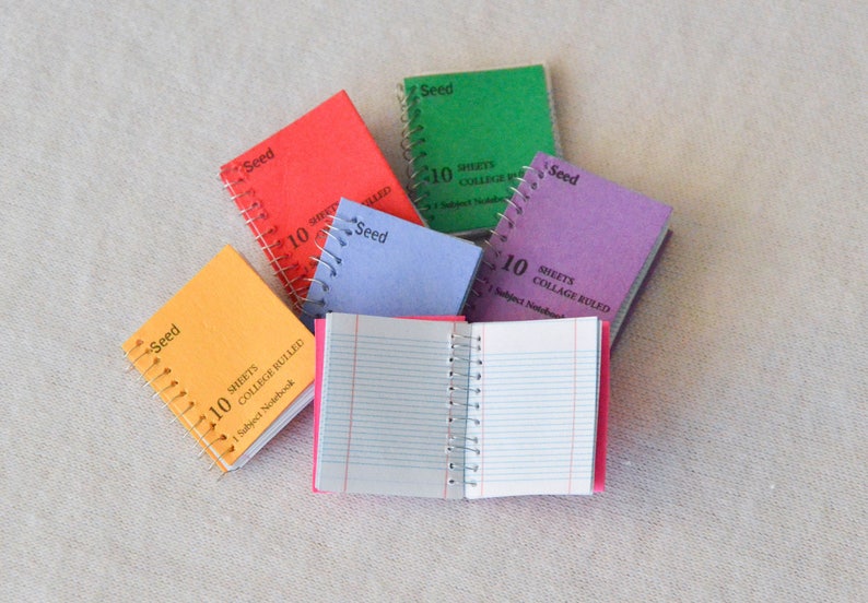 May include: A collection of six small, colorful notebooks with spiral bindings. Each notebook has the word "Seed" printed on the cover and says "10 sheets college ruled" or "10 sheets collage ruled".
