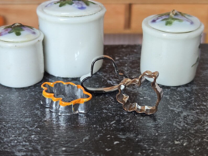 May include: Three metal cookie cutters in different shapes: a heart, a leaf, and a flower. The cutters are on a black surface.