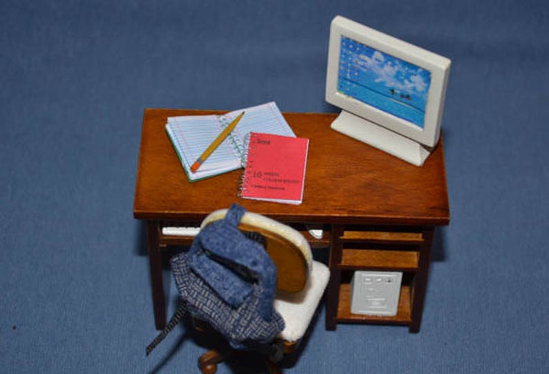 May include: A miniature wooden desk with a computer monitor, a pencil, two notebooks, and a backpack. The desk has a shelf underneath with a small white box.