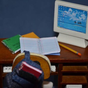 May include: A wooden desk with a computer monitor, a pencil, and three notebooks. A blue backpack with a red notebook is on the desk.