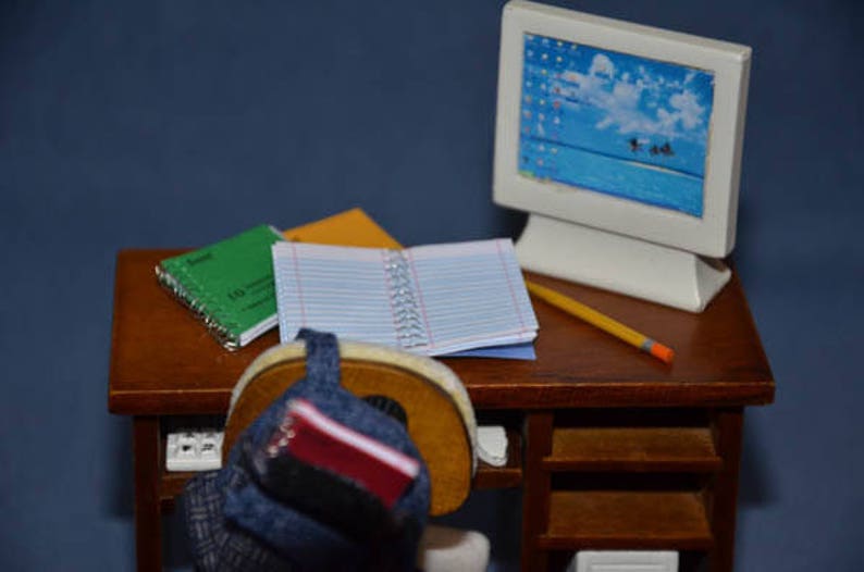 May include: A wooden desk with a computer monitor, a pencil, and three notebooks. A blue backpack with a red notebook is on the desk.