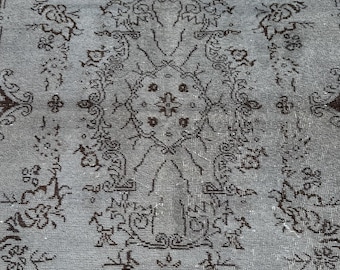 May include: A rectangular, vintage-style rug with a central floral pattern in shades of gray and brown. The rug features a detailed border and intricate designs, suitable for home decor.