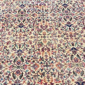 May include: An antique rug with an intricate floral pattern. The rug features a cream-colored background with a repeating design of flowers and leaves in shades of blue, pink, and green. The rug has a detailed border.