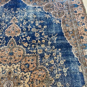 May include: A distressed, vintage-style rug with a rich navy blue central field. The rug features intricate floral and geometric patterns in shades of beige, brown, and blue. The border has a faded, antique appearance, adding to its aged charm.
