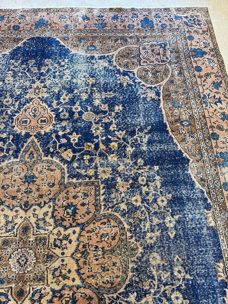 May include: A distressed, vintage-style rug with a rich navy blue central field. The rug features intricate floral and geometric patterns in shades of beige, brown, and blue. The border has a faded, antique appearance, adding to its aged charm.