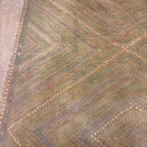 May include: A vintage rug with a geometric pattern. The rug features diagonal stripes in shades of green, gold, and lavender, with white dotted lines. The edges have a decorative border. The rug is likely made of woven material.