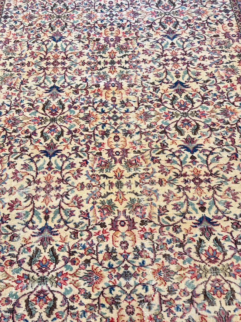 May include: An antique beige rug with an intricate floral pattern in shades of blue, pink, and green. The rug features a detailed, symmetrical design with a distressed appearance, suggesting age and use. The rug's style is reminiscent of traditional Persian or Oriental rugs.