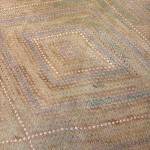 May include: Close-up of a woven textile with a geometric diamond pattern. The design features alternating diagonal stripes in shades of tan, green, and lavender, with rows of white dots. The overall texture appears soft and slightly worn.