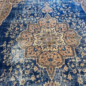May include: A large, rectangular rug with a distressed, vintage appearance. The rug features a central medallion design in shades of peach, beige, and blue, set against a deep blue background. Floral and geometric patterns are visible throughout the rug's design.
