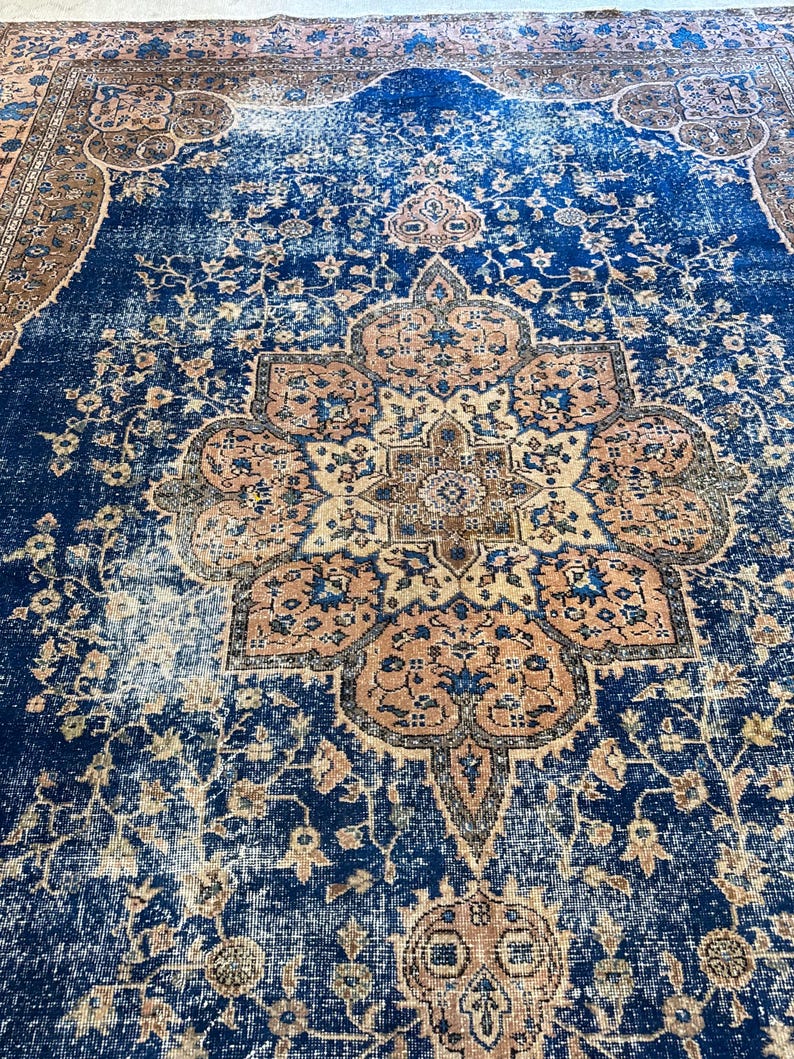 May include: A large, rectangular rug with a distressed, vintage appearance. The rug features a central medallion design in shades of peach, beige, and blue, set against a deep blue background. Floral and geometric patterns are visible throughout the rug's design.