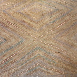 May include: A vintage rug with a geometric diamond pattern. The rug features a color palette of beige, light blue, and brown, with white dotted lines accenting the design. The edges have a fringe detail.