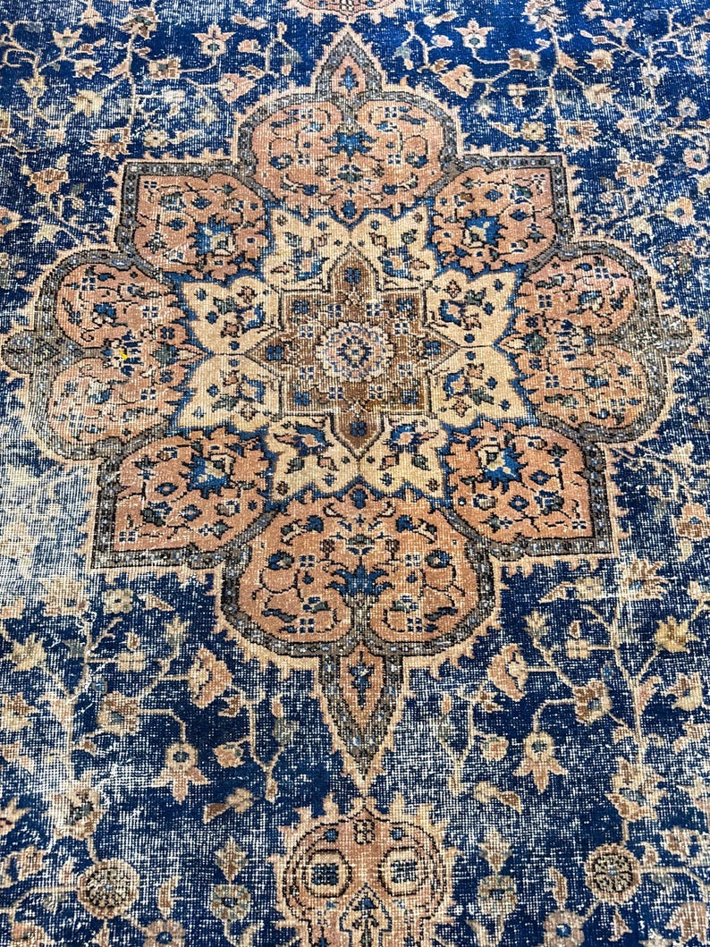May include: A detailed close-up of a vintage rug with a central medallion design. The rug features a navy blue background with a faded, distressed appearance. The medallion is a combination of peach, beige, and blue floral patterns, creating a classic, ornate aesthetic.