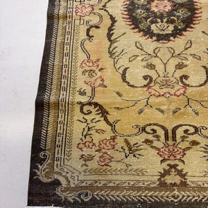 May include: Close-up of a vintage rug with a beige and brown color scheme. The rug features floral and scroll patterns in shades of brown, red, and beige. The border is a dark brown with intricate detailing. The rug has a distressed, antique appearance.