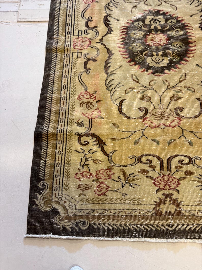 May include: Close-up of a vintage rug with a beige and brown color scheme. The rug features floral and scroll patterns in shades of brown, red, and beige. The border is a dark brown with intricate detailing. The rug has a distressed, antique appearance.