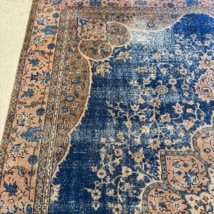May include: A section of a distressed, vintage rug with a rich, dark blue central field. The rug features a detailed floral pattern in shades of peach, brown, and blue. The border has a repeating floral design.