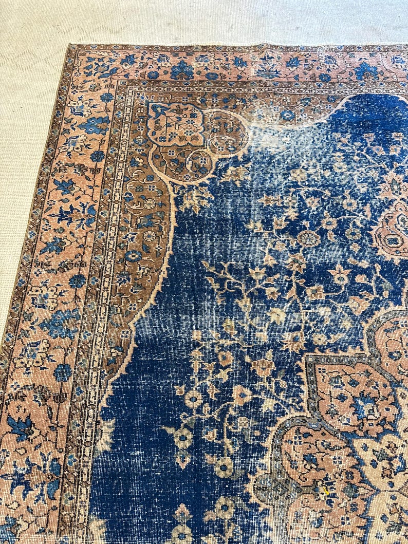 May include: A section of a distressed, vintage rug with a rich, dark blue central field. The rug features a detailed floral pattern in shades of peach, brown, and blue. The border has a repeating floral design.