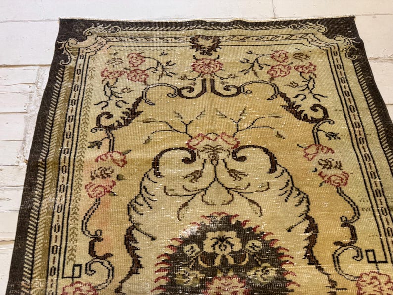 May include: An antique-style rug with a central floral design in shades of beige, brown, and pink. The rug features an ornate border and a detailed pattern, creating a vintage aesthetic. The rug's design includes floral and geometric elements.