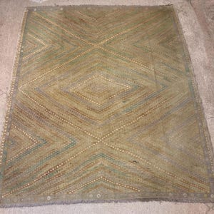May include: A rectangular rug with a geometric diamond pattern. The rug features a color palette of muted greens, browns, and beige. The design includes intersecting lines and diamond shapes, creating a textured appearance. The rug has a fringe border.