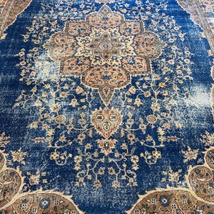 May include: A distressed, vintage-style rug with a central medallion design. The rug features a deep blue field with faded areas, and a border in shades of brown and peach. Floral and geometric patterns are visible throughout the rug's surface.