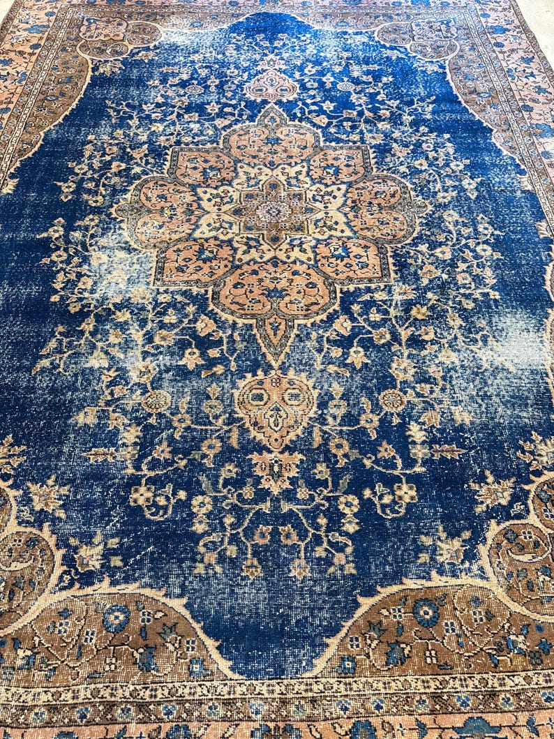 May include: A distressed, vintage-style rug with a central medallion design. The rug features a deep blue field with faded areas, and a border in shades of brown and peach. Floral and geometric patterns are visible throughout the rug's surface.