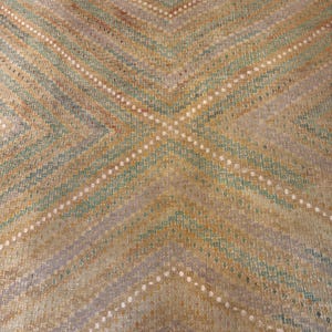 May include: A close-up of a woven rug with a geometric pattern. The rug features a repeating design of diagonal lines in shades of tan, green, and blue, with white dotted accents. The rug has a fringed edge.