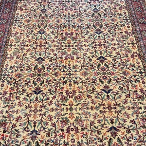 May include: An antique area rug with an intricate floral pattern in cream, red, blue, and purple. The rug features a detailed border and a dense, all-over design. The rug's aged appearance suggests it is vintage.