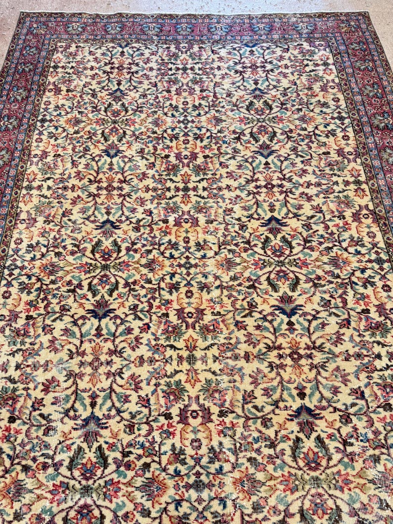 May include: An antique area rug with an intricate floral pattern in cream, red, blue, and purple. The rug features a detailed border and a dense, all-over design. The rug's aged appearance suggests it is vintage.