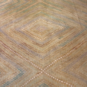 May include: Close-up of a woven rug with a diamond pattern. The rug features a color palette of tan, blue, and white. The design includes intersecting diagonal lines and diamond shapes, creating a textured appearance.