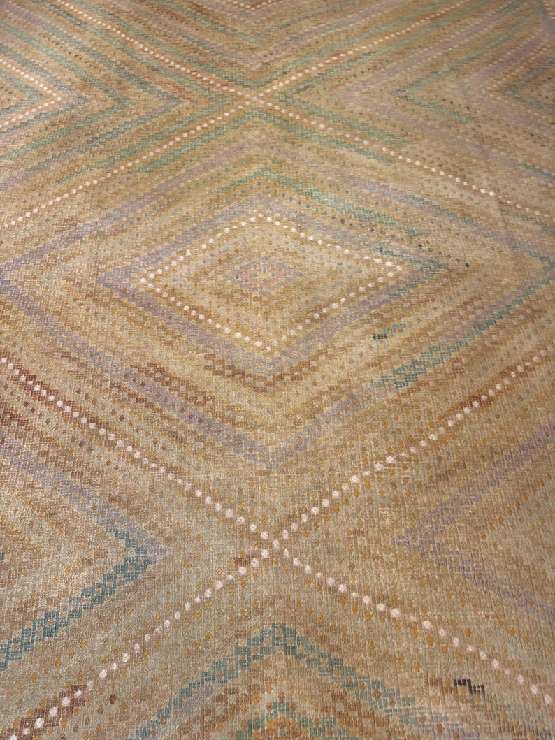 May include: Close-up of a woven rug with a diamond pattern. The rug features a color palette of tan, blue, and white. The design includes intersecting diagonal lines and diamond shapes, creating a textured appearance.