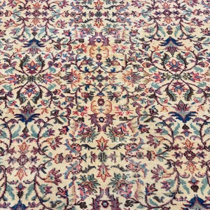 May include: Cream-colored area rug with an intricate floral pattern in shades of blue, purple, pink, and green. The rug features a detailed, symmetrical design, creating a vintage or antique aesthetic. The rug's texture appears soft and inviting.