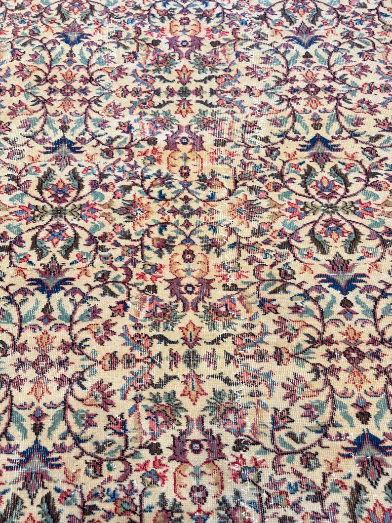 May include: Cream-colored area rug with an intricate floral pattern in shades of blue, purple, pink, and green. The rug features a detailed, symmetrical design, creating a vintage or antique aesthetic. The rug's texture appears soft and inviting.
