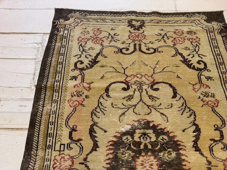 May include: An antique rug with a beige field and a dark brown border. The rug features a floral pattern in shades of red and brown, with intricate details and a distressed appearance. The rug is rectangular and appears to be made of woven material.