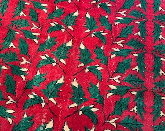May include: A woven textile rug featuring a vibrant red background decorated with a repeating pattern of dark green holly leaves and small cream-colored accents arranged in vertical columns across the entire surface of the fabric.