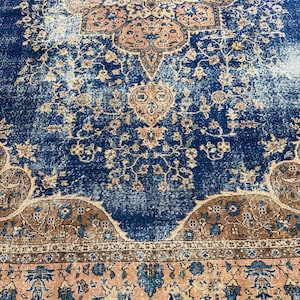 May include: A distressed, vintage-style rug with a rich navy blue central field. The rug features intricate floral and geometric patterns in shades of peach, brown, and cream. The design includes a detailed border.