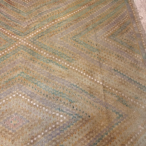 May include: A vintage rug with a geometric pattern. The rug features a beige background with diagonal stripes in shades of brown, green, and purple. White dots accent the design. The rug has a fringed edge.