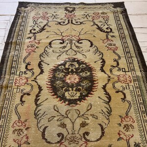 May include: An antique beige rug with a central medallion design and floral motifs. The rug features a dark brown border and accents in red and black. The intricate pattern and faded appearance suggest a vintage origin, adding a touch of elegance to any space.