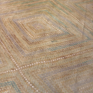 May include: A close-up of a rug with a geometric diamond pattern. The rug features a color palette of tan, brown, and blue-green hues. The design includes diagonal lines and diamond shapes, creating a textured appearance. The rug's construction appears to be woven.