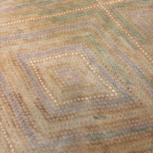 May include: Close-up of a woven textile with a geometric diamond pattern. The design features alternating bands of tan, light blue, and lavender hues, accented with rows of white dots. The overall texture appears soft and inviting.