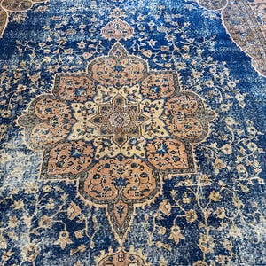 May include: A distressed, vintage-style rug with a central medallion design. The rug features a deep blue field with intricate floral patterns in shades of beige and rust. The edges have a faded appearance, adding to its antique aesthetic.