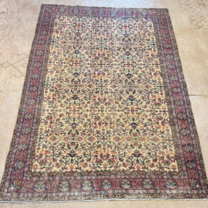May include: An antique Persian rug with a cream-colored field and an intricate floral pattern in shades of red, blue, green, and gold. The rug has a detailed border in red and cream.