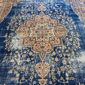 May include: A large, rectangular rug with a distressed, vintage appearance. The rug features a deep blue central field with a central medallion and floral patterns in shades of peach, tan, and brown. The border is a complementary color palette.