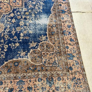 May include: A distressed, rectangular rug with a central blue field and intricate floral patterns in shades of brown and peach. The rug has a faded, vintage appearance, with a detailed border.