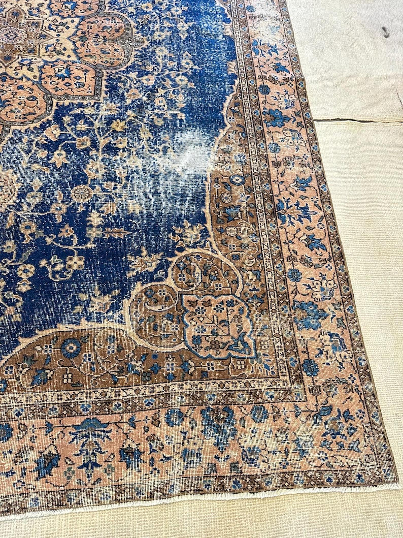 May include: A distressed, rectangular rug with a central blue field and intricate floral patterns in shades of brown and peach. The rug has a faded, vintage appearance, with a detailed border.