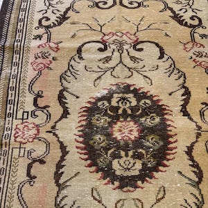 May include: A vintage beige rug with a central medallion design. The rug features a floral pattern in shades of red, brown, and green, with a dark brown border. The rug's design is intricate and detailed, with a distressed appearance.