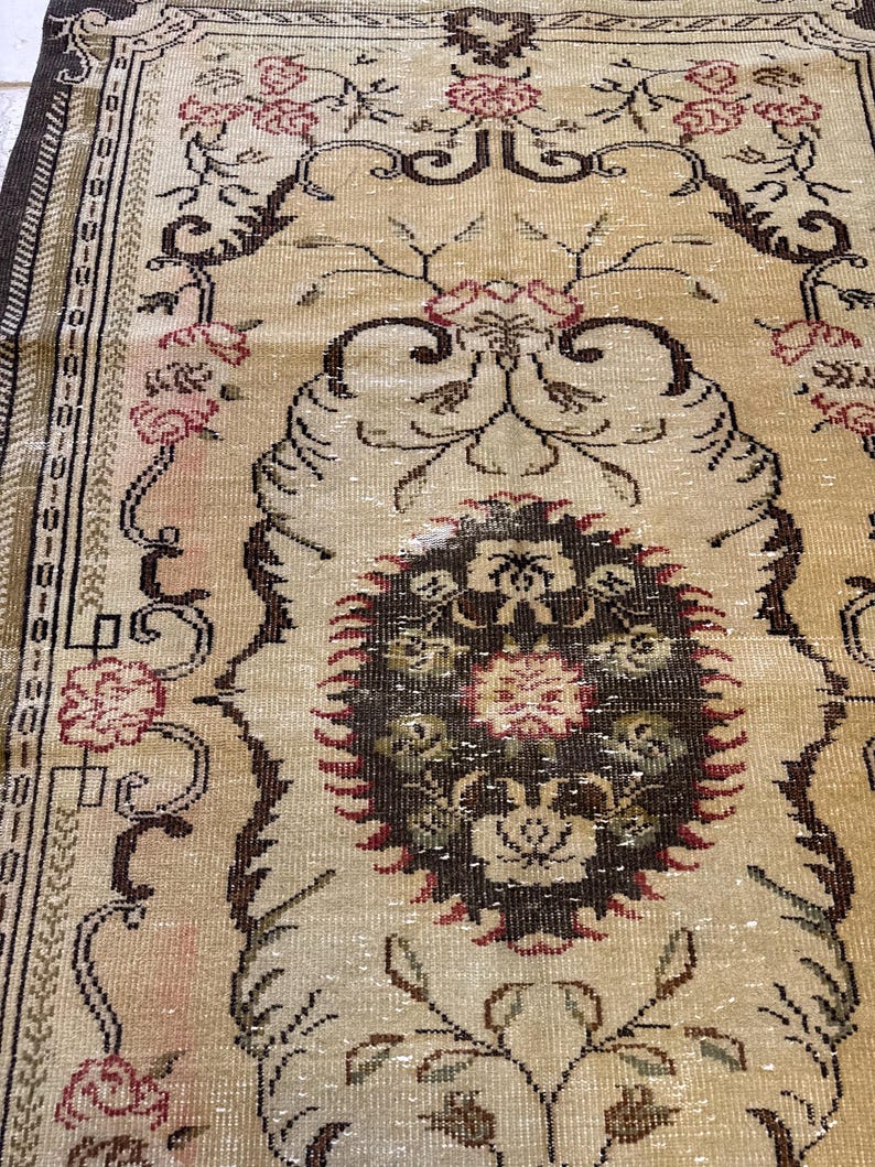 May include: A vintage beige rug with a central medallion design. The rug features a floral pattern in shades of red, brown, and green, with a dark brown border. The rug's design is intricate and detailed, with a distressed appearance.